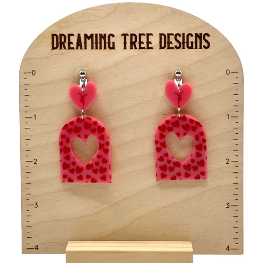 a pair of pink heart shaped earrings sitting on top of a wooden stand